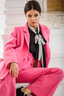 Pembe takım elbise ve lüks ev iç merdiven üzerinde oturan siyah t-shirt giyen güzel esmer kadın portresi stüdyo 