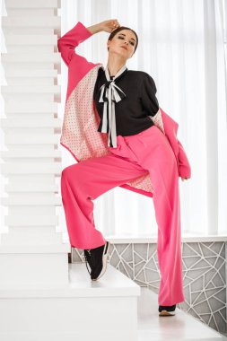 Pembe takım elbise ve lüks ev iç merdiven üzerinde duran siyah t-shirt giyen güzel esmer kadın portresi stüdyo 