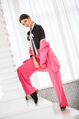 Pembe takım elbise ve lüks ev iç merdiven üzerinde duran siyah t-shirt giyen güzel esmer kadın portresi stüdyo 