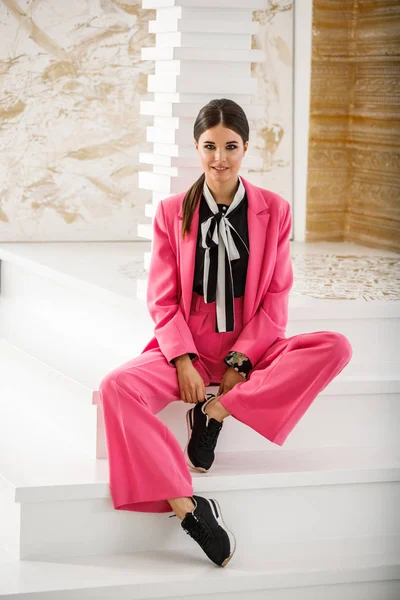 Pembe takım elbise ve lüks ev iç merdiven üzerinde oturan siyah t-shirt giyen güzel esmer kadın portresi stüdyo 