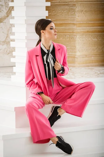 Pembe takım elbise ve lüks ev iç merdiven üzerinde oturan siyah t-shirt giyen güzel esmer kadın portresi stüdyo 