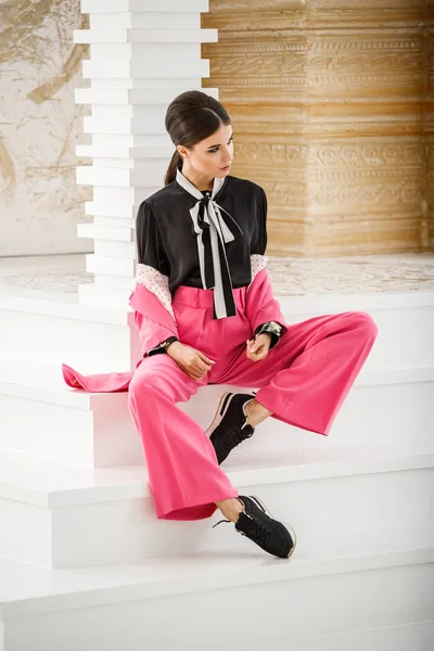 Pembe takım elbise ve lüks ev iç merdiven üzerinde oturan siyah t-shirt giyen güzel esmer kadın portresi stüdyo 