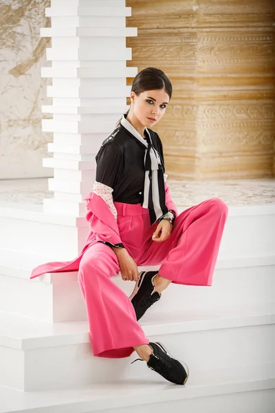 Pembe takım elbise ve lüks ev iç merdiven üzerinde oturan siyah t-shirt giyen güzel esmer kadın portresi stüdyo 