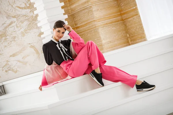 Pembe takım elbise ve lüks ev iç merdiven üzerinde oturan siyah t-shirt giyen güzel esmer kadın portresi stüdyo 