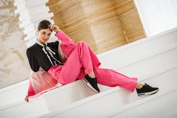 Pembe takım elbise ve lüks ev iç merdiven üzerinde oturan siyah t-shirt giyen güzel esmer kadın portresi stüdyo 