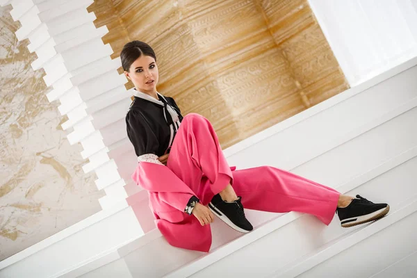 Pembe takım elbise ve lüks ev iç merdiven üzerinde oturan siyah t-shirt giyen güzel esmer kadın portresi stüdyo 