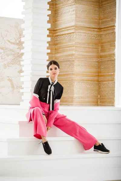 Pembe takım elbise ve lüks ev iç merdiven üzerinde oturan siyah t-shirt giyen güzel esmer kadın portresi stüdyo 