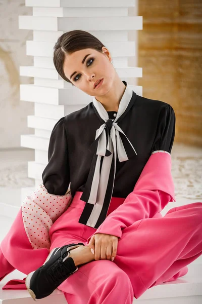 Pembe takım elbise ve lüks ev iç merdiven üzerinde oturan siyah t-shirt giyen güzel esmer kadın portresi stüdyo 