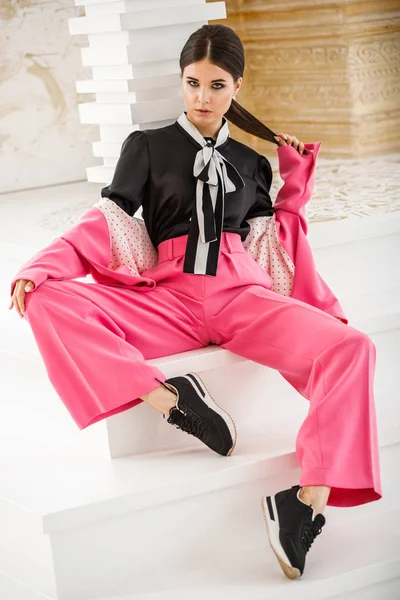 Pembe takım elbise ve lüks ev iç merdiven üzerinde oturan siyah t-shirt giyen güzel esmer kadın portresi stüdyo 