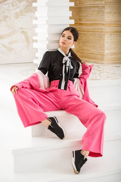 Pembe takım elbise ve lüks ev iç merdiven üzerinde oturan siyah t-shirt giyen güzel esmer kadın portresi stüdyo 