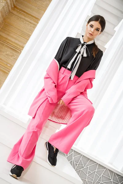 Pembe takım elbise ve lüks ev iç merdiven üzerinde duran siyah t-shirt giyen güzel esmer kadın portresi stüdyo 