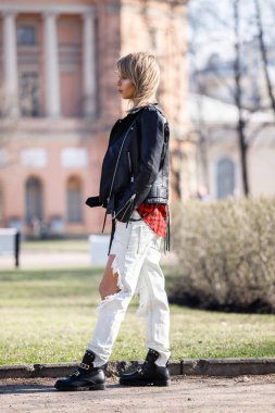 Güzellik Sarışın kadın giyen siyah deri ceket, gri t-shirt ve yırtık kot park, bulanık şehir arka plan ayakta açık portresi 