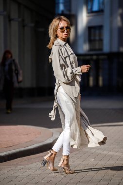 Açık bej ceket, beyaz gömlek ve beyaz pantolon giyiyor, bulanık arka planda bina ile sokakta duran güzellik kadın portresi