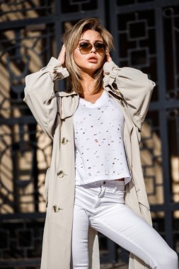 Açık bej ceket, beyaz gömlek ve beyaz pantolon giyiyor, bulanık arka planda bina ile sokakta duran güzellik kadın portresi