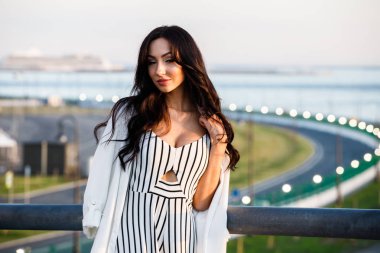 Çizgili siyah beyaz elbiseli güzel genç esmer kadın açık bir kadeh. Güneş ışığı, şehir dolgu üzerinde duran kıvırcık kadın şehir görünümü arka plan bulanık 