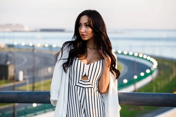 Çizgili siyah beyaz elbiseli güzel genç esmer kadın açık bir kadeh. Güneş ışığı, şehir dolgu üzerinde duran kıvırcık kadın şehir görünümü arka plan bulanık 
