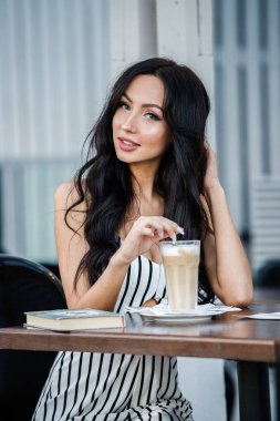 Çizgili siyah beyaz elbiseli güzel genç esmer kadın portresi. Kahve içme ve kafe iç kitap okuma kıvırcık kadın