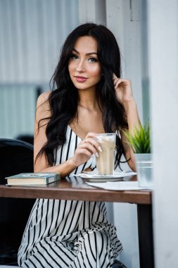 Çizgili siyah beyaz elbiseli güzel genç esmer kadın portresi. Kahve içme ve kafe iç kitap okuma kıvırcık kadın