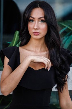 Portre portre ile şık makyaj, yeşil bitkiler arka plan siyah elbiseli güzel genç esmer kadının