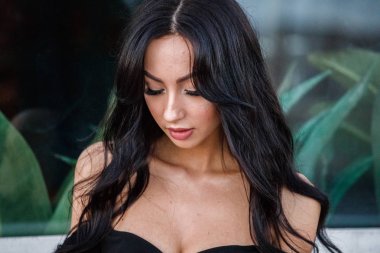 Portre portre ile şık makyaj, yeşil bitkiler arka plan siyah elbiseli güzel genç esmer kadının