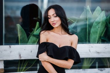 Portre portre ile şık makyaj, yeşil bitkiler arka plan siyah elbiseli güzel genç esmer kadının