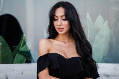 Portre portre ile şık makyaj, yeşil bitkiler arka plan siyah elbiseli güzel genç esmer kadının