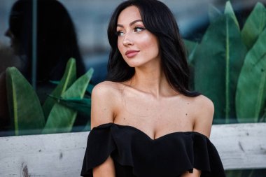 Portre portre ile şık makyaj, yeşil bitkiler arka plan siyah elbiseli güzel genç esmer kadının