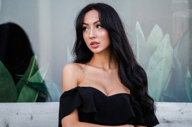 Portre portre ile şık makyaj, yeşil bitkiler arka plan siyah elbiseli güzel genç esmer kadının