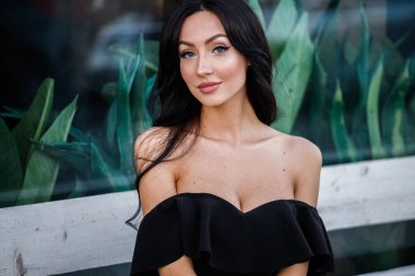 Portre portre ile şık makyaj, yeşil bitkiler arka plan siyah elbiseli güzel genç esmer kadının