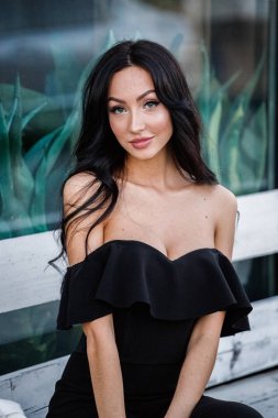 Portre portre ile şık makyaj, yeşil bitkiler arka plan siyah elbiseli güzel genç esmer kadının