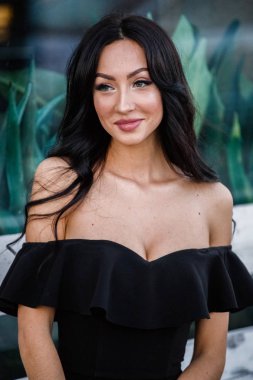 Portre portre ile şık makyaj, yeşil bitkiler arka plan siyah elbiseli güzel genç esmer kadının