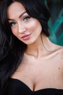 Portre portre ile şık makyaj, yeşil bitkiler arka plan siyah elbiseli güzel genç esmer kadının