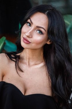 Portre portre ile şık makyaj, yeşil bitkiler arka plan siyah elbiseli güzel genç esmer kadının