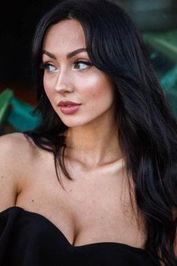 Portre portre ile şık makyaj, yeşil bitkiler arka plan siyah elbiseli güzel genç esmer kadının