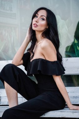 Yeşil bitkiler arka plan tahta bankta oturan şık makyaj ile siyah elbiseli güzel genç esmer kadın portresi