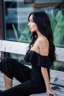 Yeşil bitkiler arka plan tahta bankta oturan şık makyaj ile siyah elbiseli güzel genç esmer kadın portresi