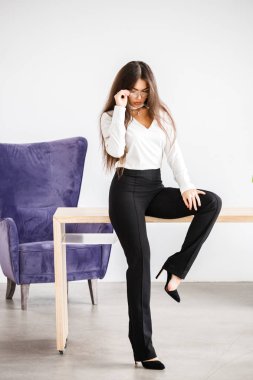 Stüdyo portre genç esmer kadının beyaz gömlek ve siyah pantolon. Ofis iç masada oturan güzellik iş kadın