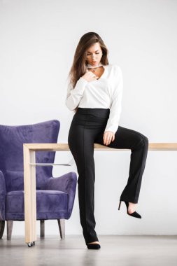 Stüdyo portre genç esmer kadının beyaz gömlek ve siyah pantolon. Ofis iç masada oturan güzellik iş kadın
