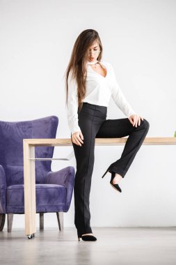 Stüdyo portre genç esmer kadının beyaz gömlek ve siyah pantolon. Ofis iç masada oturan güzellik iş kadın