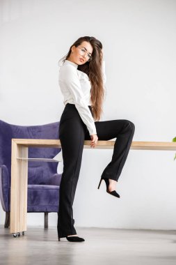 Stüdyo portre genç esmer kadının beyaz gömlek ve siyah pantolon. Ofis iç masada oturan güzellik iş kadın