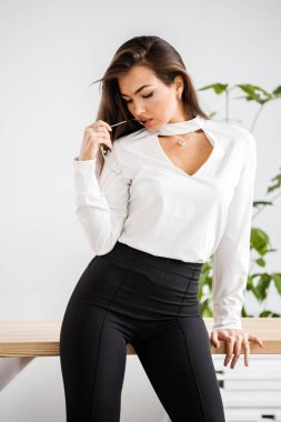 Stüdyo portre genç esmer kadının beyaz gömlek ve siyah pantolon. Ofis iç masada oturan güzellik iş kadın