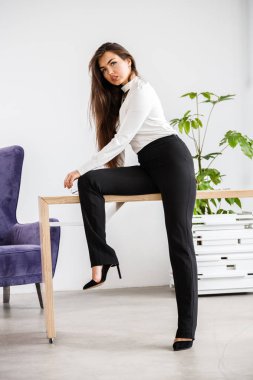 Stüdyo portre genç esmer kadının beyaz gömlek ve siyah pantolon. Ofis iç masada oturan güzellik iş kadın