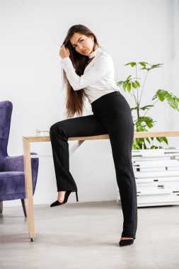 Stüdyo portre genç esmer kadının beyaz gömlek ve siyah pantolon. Ofis iç masada oturan güzellik iş kadın