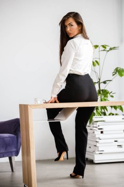 Stüdyo portre genç esmer kadının beyaz gömlek ve siyah pantolon. Ofis iç masada oturan güzellik iş kadın