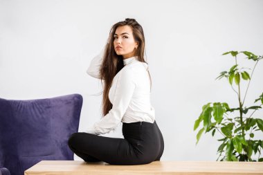 Stüdyo portre genç esmer kadının beyaz gömlek ve siyah pantolon. Ofis iç masada oturan güzellik iş kadın