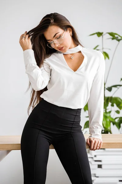 工作室肖像的年轻黑发妇女在白色衬衫和黑色裤子 美容商务妇女坐在桌在办公室内部 — 图库照片