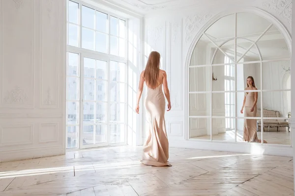 时装拍摄的美丽的金发女子在米色礼服站立反对白色内部背景 — 图库照片