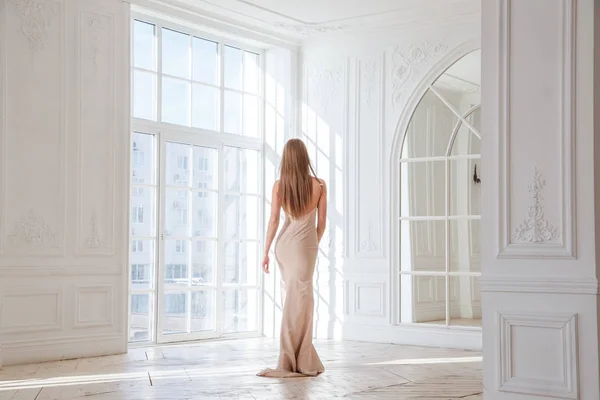 时装拍摄的美丽的金发女子在米色礼服站立反对白色内部背景 — 图库照片