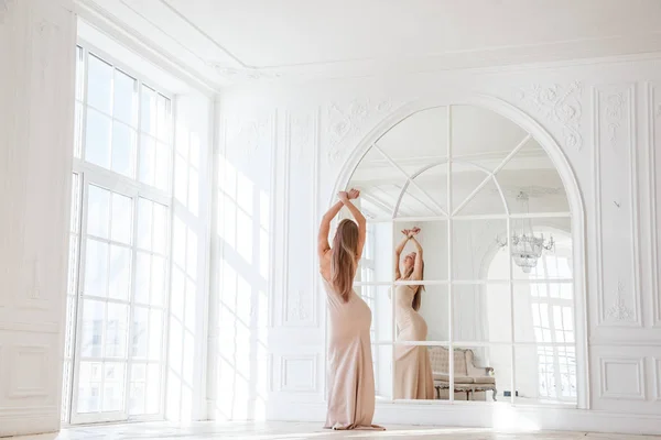 ベージュの美しい金髪女性のファッション撮影ドレス ホワイト インテリアの背景に立っています — ストック写真