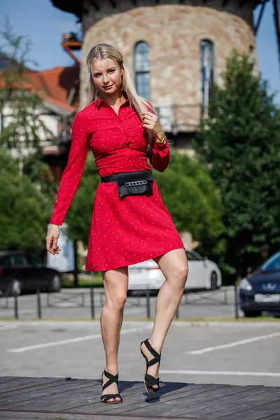 Gündüz caddenin üzerinde kırmızı elbise duran güzel sarışın kadın portresi açık moda